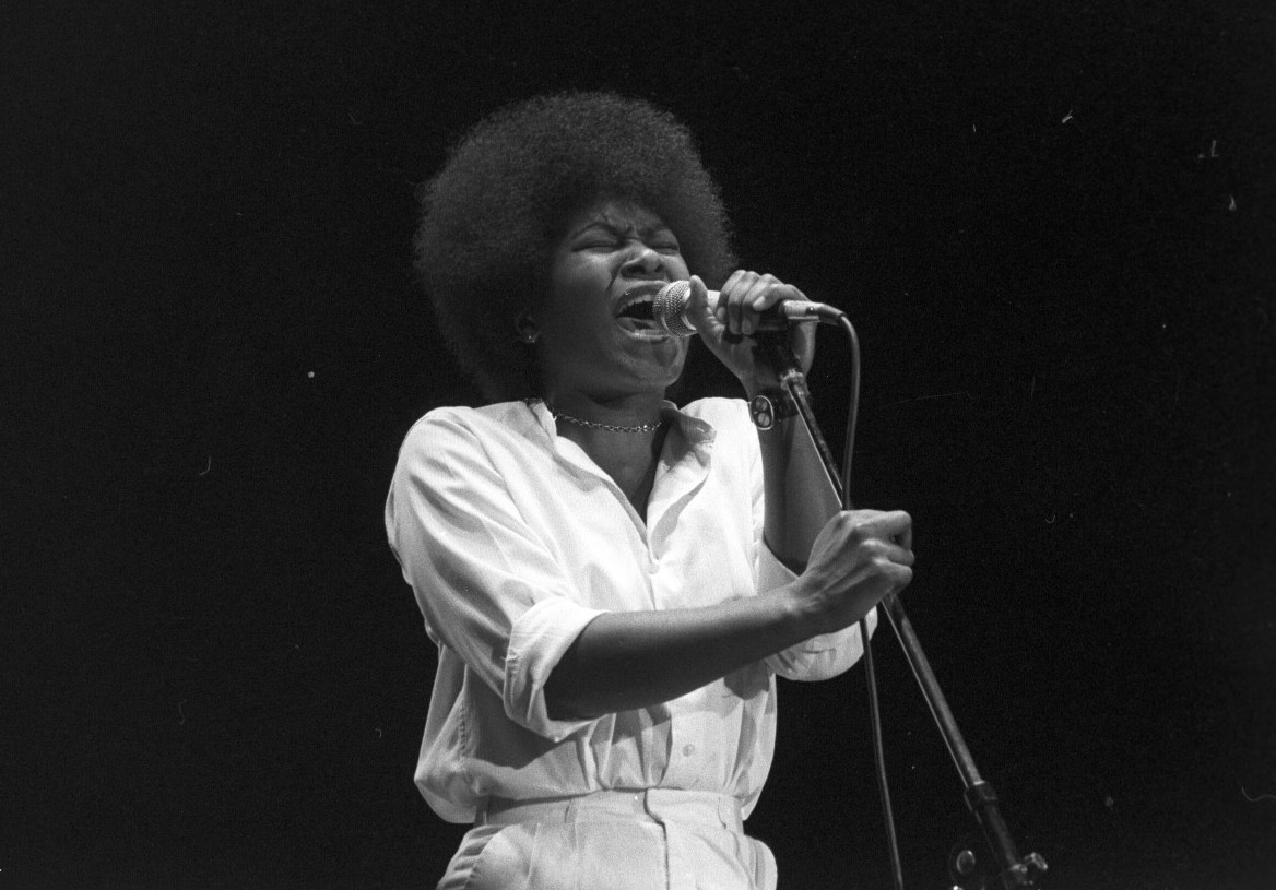 Joan Armatrading singing into a microphone on stage in Zurich in 1980.