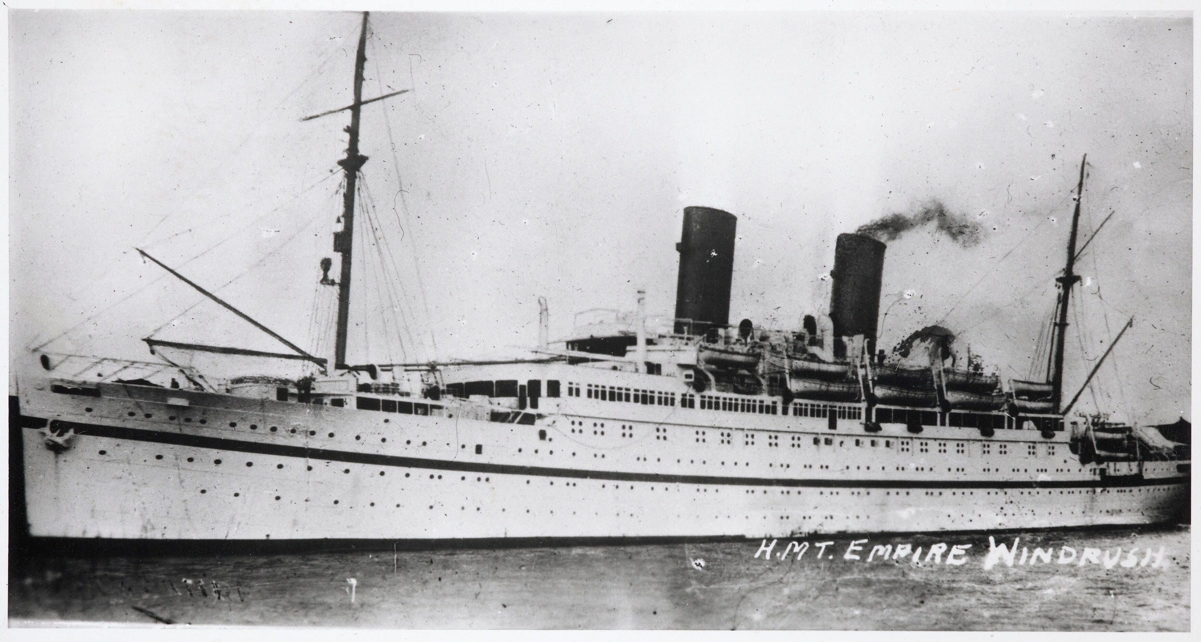 A black-and-white archival photograph of HMT Empire Windrush, a large white ship with two dark funnels.